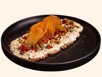 Creamy spread topped with sliced chips and garnishes on a black plate.