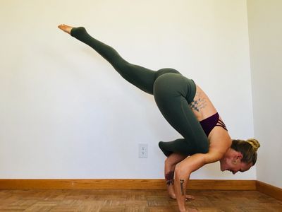 Woman performing advanced yoga arm balance pose indoors.