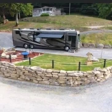 A motorhome parked on a gravel driveway near a small fenced garden with stone walls.