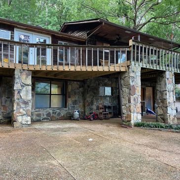 Rustic stone and wood house with elevated deck surrounded by trees.