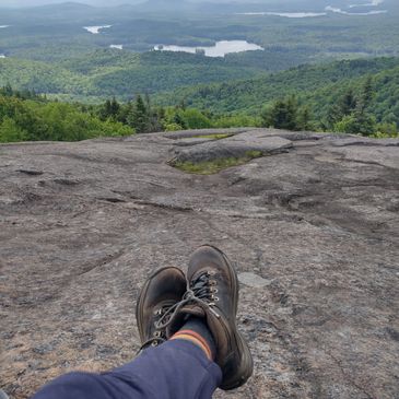 Person relaxing on a rocky mountain with a scenic forest and lake view.