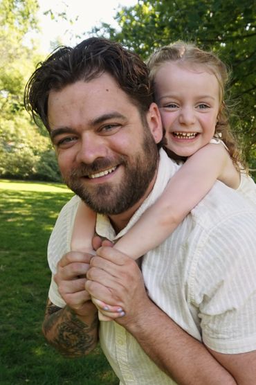 Father giving daughter a piggyback ride outdoors, both smiling joyfully.