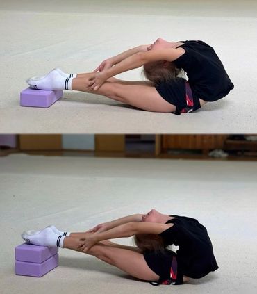A young girl stretches deeply using yoga blocks for support on her feet.