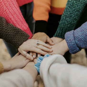 Diverse group uniting with hands together in colorful sweaters.