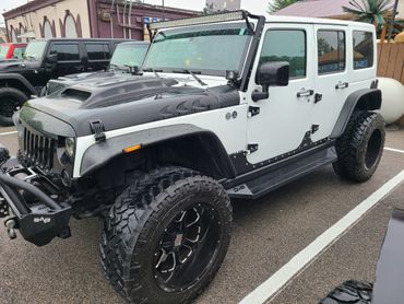 Customized black and white Jeep Wrangler with large off-road tires and rain droplets.