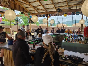 People enjoying drinks and food at an outdoor bar with hanging lanterns.