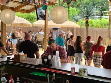People socializing at an outdoor bar with tropical decor and hanging lanterns.
