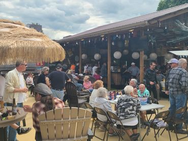 People socializing at an outdoor bar with wooden decor and thatched umbrellas.