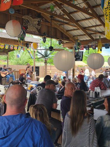 Crowded outdoor bar with live band and festive decorations.
