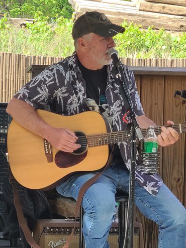 Man playing acoustic guitar and singing into a microphone on stage.