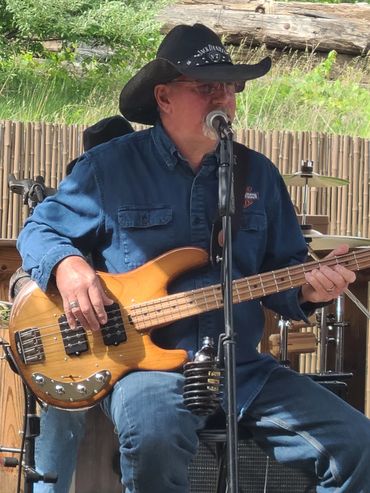 Musician in cowboy hat plays bass guitar and sings outdoors.