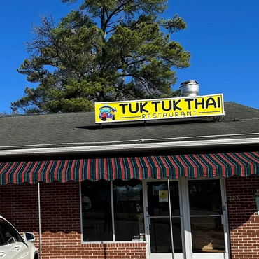 Exterior view of Tuk Tuk Thai restaurant with a striped awning and clear blue sky.