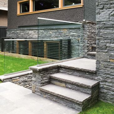 Modern outdoor stone stairs with glass railing and green lawn.