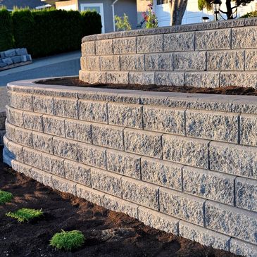 Newly constructed tiered retaining wall with soil and small plants.