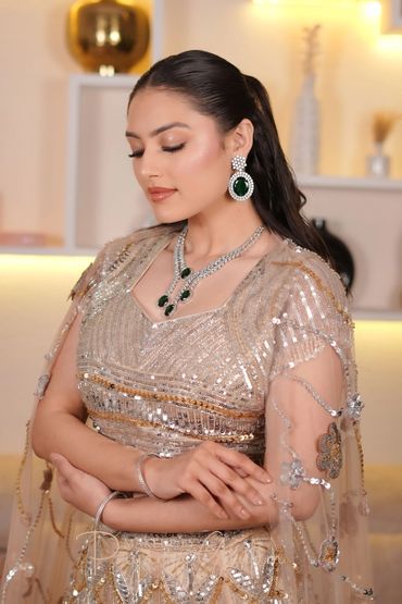 Elegant woman in a sparkling beige dress with green gemstone jewelry.