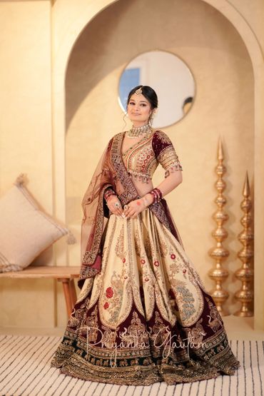 A woman in a richly embroidered traditional outfit stands gracefully indoors.