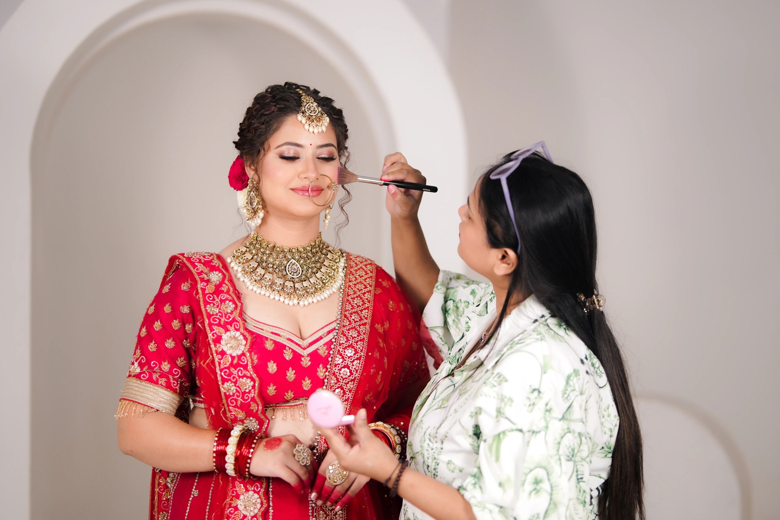 Bride getting makeup applied by a makeup artist in traditional attire.