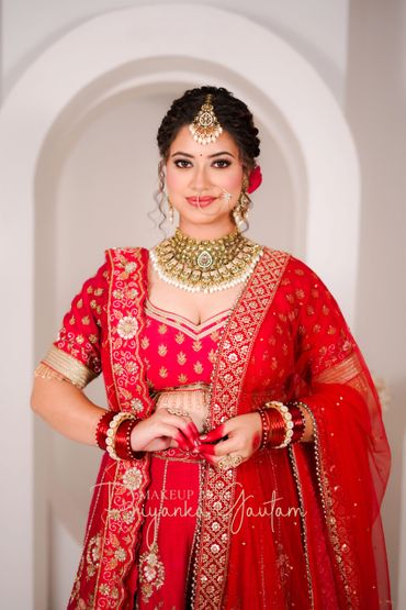 Bride in red traditional Indian attire with intricate jewelry and henna on hands.
