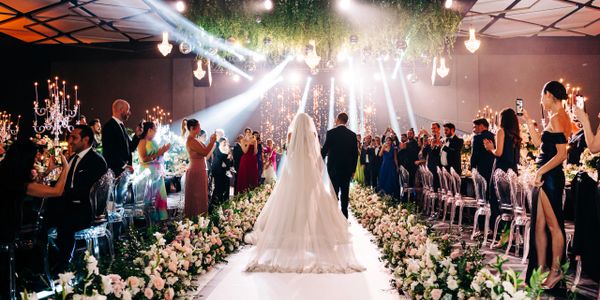 Bride and groom walk down a flower-lined aisle as guests capture the moment.