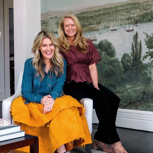 Two women smiling in a stylish living room with a scenic mural.