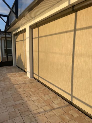 Outdoor patio with beige roller shades and tiled floor in warm sunlight.