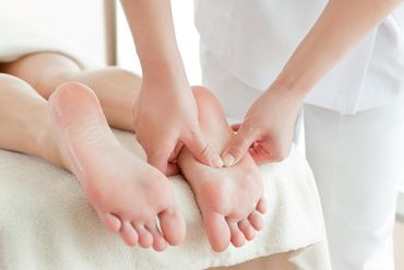 A person enjoys a deep tissue foot massage while lying on a white towel in a bright room.