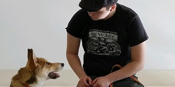 A man wearing black kneels next to a young Malamute mix
