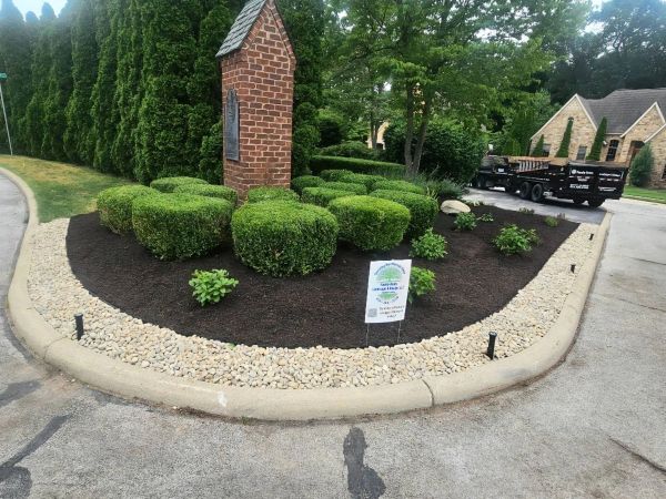 Well-manicured bushes around a brick monument in a residential neighborhood.