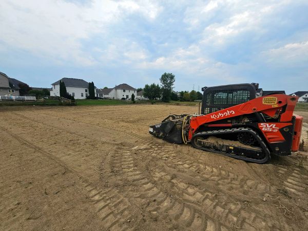 Kubota construction vehicle on a cleared dirt field near houses under a cloudy sky.