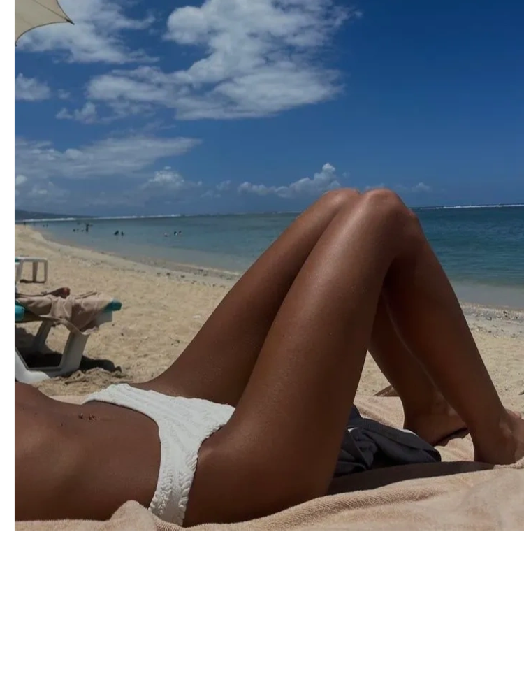 Person sunbathing on a beach in white swimwear.