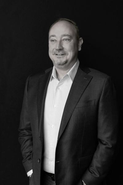 Man in suit smiling against a black background.