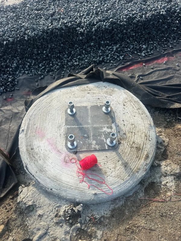 Concrete foundation base with bolts and red string on construction site.