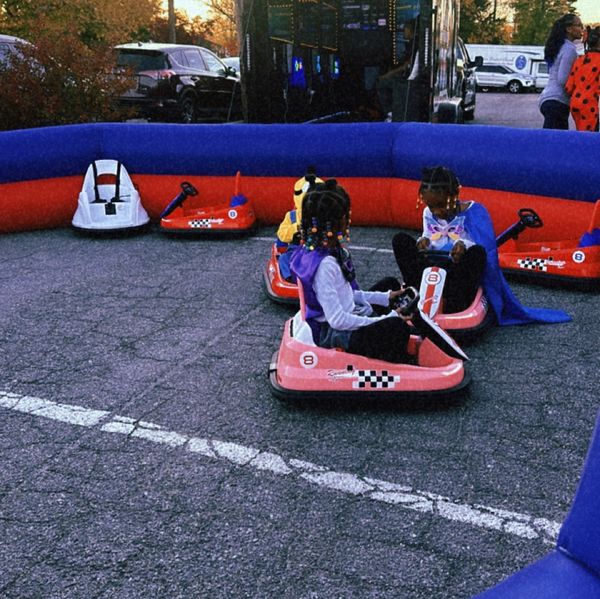 Children playing on small go-karts inside a blue and red inflatable barrier.