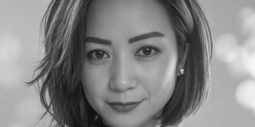 Close-up portrait of a woman with short hair against a soft pink background.