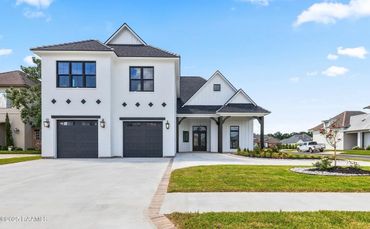 Modern white two-story house with black garage doors and neatly trimmed lawn.