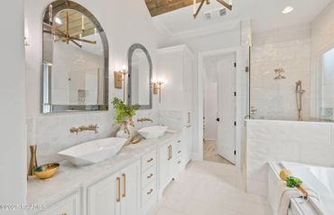 Bright, modern bathroom with dual sinks, gold fixtures, and a glass-enclosed shower.