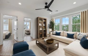 Bright living room with cream sectional sofa and blue cushions, featuring large windows and wooden furniture.