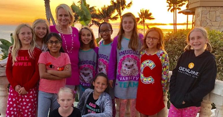 A group of smiling kids and an adult posing at sunset near palm trees.