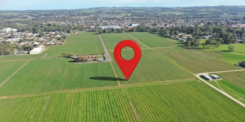 Aerial view of farmland with a large red location pin in the center.