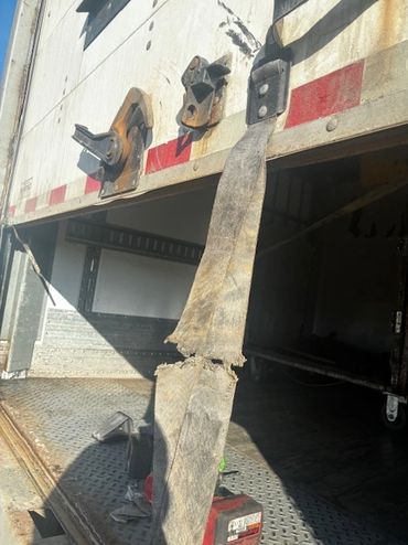 Worn and torn strap hanging from a truck trailer's open door.