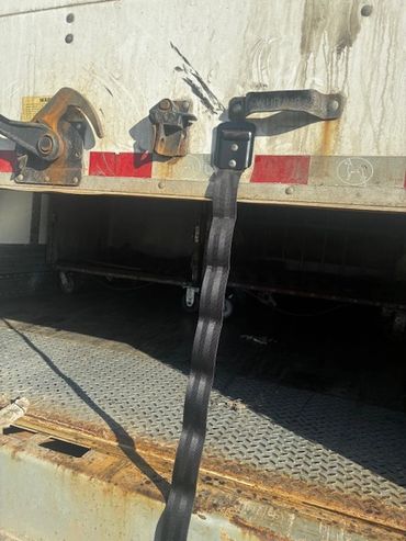 A black strap hangs from the back of a rusty, open truck trailer.