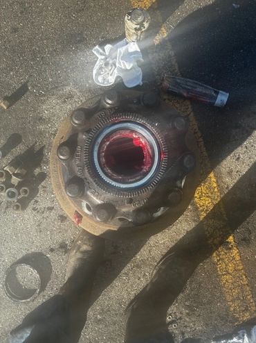 Disassembled vehicle wheel hub with grease and tools on asphalt.