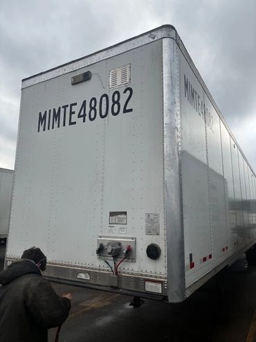 A large white trailer with the ID MIMTE48082 under a cloudy sky.