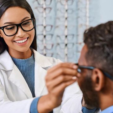 Optometrist fitting eyeglasses on a patient with a smile.