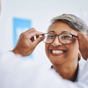 A smiling woman trying on new eyeglasses with assistance.
