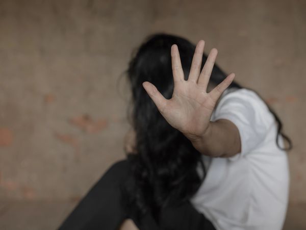 Woman sitting on the floor hiding her face and holding her arm and hand out pushing the viewer away.