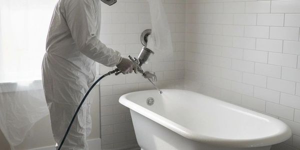 Person in protective suit spraying disinfectant in a white bathroom.