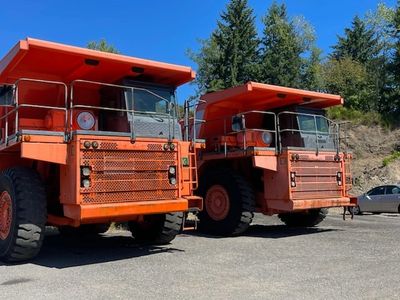 Two large orange mining trucks parked side by side under clear blue sky.