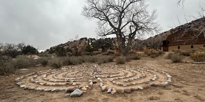 Stone labyrinth on barren ground under cloudy sky near a building.