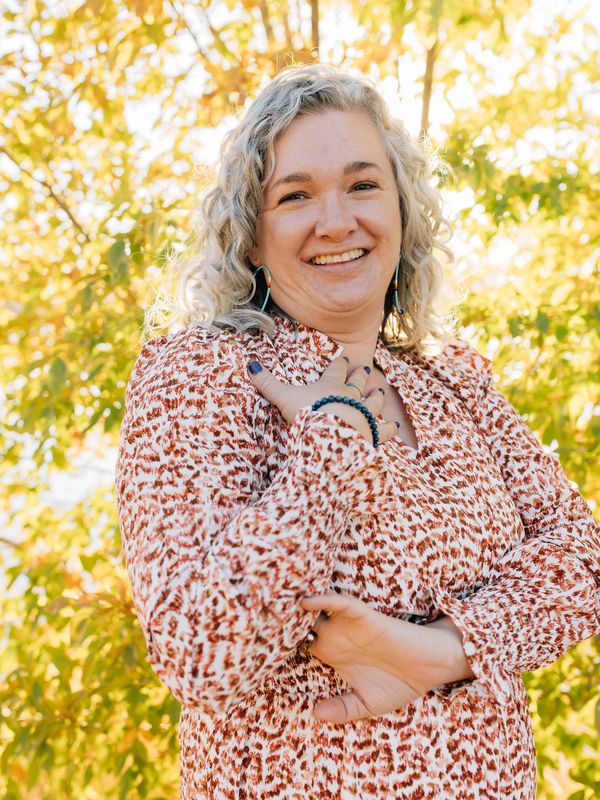 Smiling woman with curly hair in patterned dress posing outdoors in autumn.